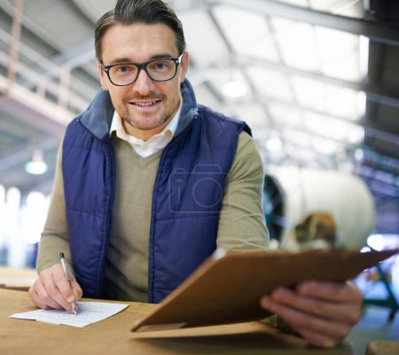 Photo for Ive got your order right here. Portrait of a smiling manager reading paperwork while standing on the factory floor - Royalty Free Image