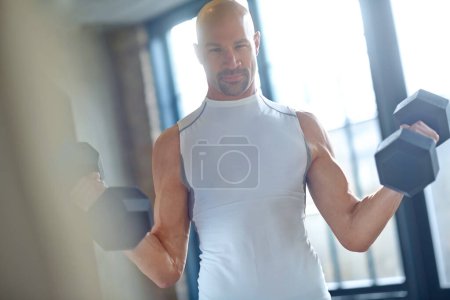 Foto de Afinando su máquina. Retrato de un joven guapo con una cabeza afeitada levantando pesas en el gimnasio - Imagen libre de derechos