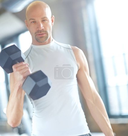 Foto de Su vida es el gimnasio. un joven guapo con una cabeza afeitada levantando pesas en el gimnasio - Imagen libre de derechos