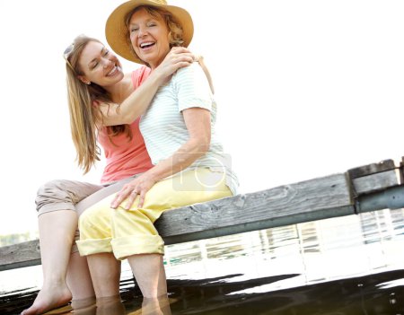 Téléchargez les photos : Sourires d'été. Une femme mûre embrassant sa mère assis sur une jetée au bord du lac - en image libre de droit