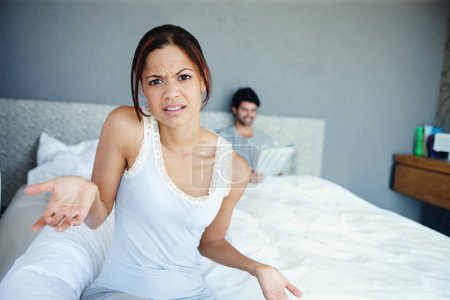 Téléchargez les photos : Que dois-je faire maintenant ? Portrait d'une femme confuse assise sur le côté de son lit avec son petit ami en arrière-plan - en image libre de droit