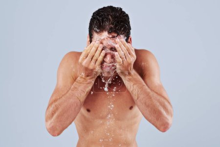 Téléchargez les photos : Nettoyage ultime. Studio plan d'un jeune homme à poitrine nue éclaboussant d'eau sur son visage - en image libre de droit