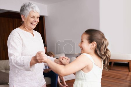 Téléchargez les photos : Tenant la main, dansant ou heureuse grand-mère avec un enfant jouant ou riant avec joie dans la maison familiale. Grand-mère dansant, enfant souriant ou drôle vieille femme relaxant ou collant ensemble dans la retraite ou la maison. - en image libre de droit
