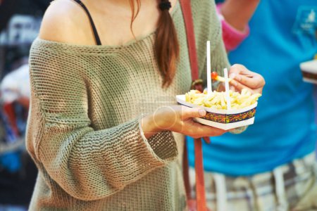 Téléchargez les photos : La nourriture du festival. une jeune femme mangeant des frites lors d'un festival en plein air - en image libre de droit