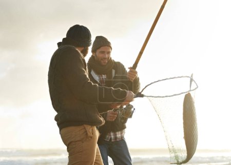 Foto de Atrapando al grande. dos jóvenes pescando en la playa - Imagen libre de derechos