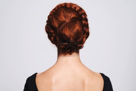 Braids and buns. Studio shot of a redhead woman with a braided up-do posing against a gray background