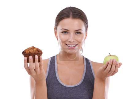 Photo for Trying to make the healthy choice. A young woman holding a muffin in one hand and an apple in the other - Royalty Free Image