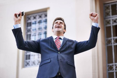Téléchargez les photos : Je suis riche. un homme d'affaires ravi levant les bras en victoire devant un immeuble de la ville - en image libre de droit