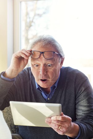 Foto de Algunas cosas en Internet te sorprenderán. un hombre mayor usando una tableta en casa - Imagen libre de derechos