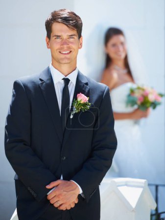 Photo for They make a great team. A handsome young groom smiling at you while his wife-to-be stands blurred in the background - Royalty Free Image