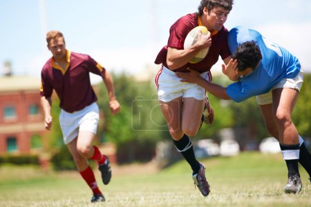 Foto de Atrapado a mitad de acción. Tiro de longitud completa de un joven jugador de rugby tratando de evitar un tackle - Imagen libre de derechos