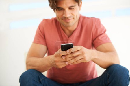 Téléchargez les photos : Connectivité facile. Un beau jeune homme lisant un SMS sur son téléphone - en image libre de droit