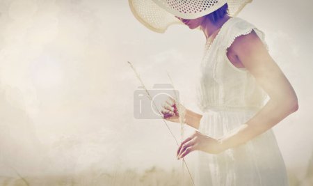 Téléchargez les photos : Entrer en contact avec ses racines. Une femme debout dans un champ tenant une tige de blé - en image libre de droit