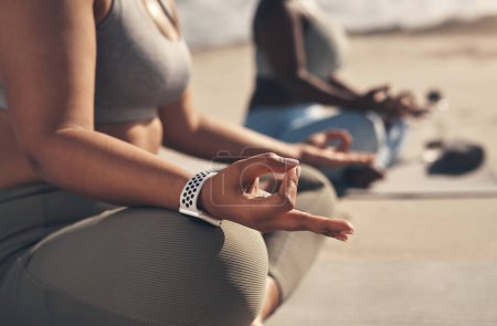 Téléchargez les photos : Le yoga vous apprend à être patient avec vous-même. deux jeunes femmes méditant pendant leur routine de yoga sur la plage - en image libre de droit
