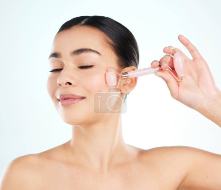 Photo for Pamper time for her face. Studio shot of an attractive young woman using a face massager against a light background - Royalty Free Image