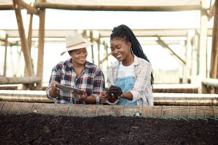 Foto de Dos agricultores controlan la calidad del suelo. Granjero afroamericano sosteniendo tierra. Dos colegas revisando la calidad del suelo en una granja. Granjeros felices usando una tableta digital. Dos mujeres trabajando en una granja. - Imagen libre de derechos