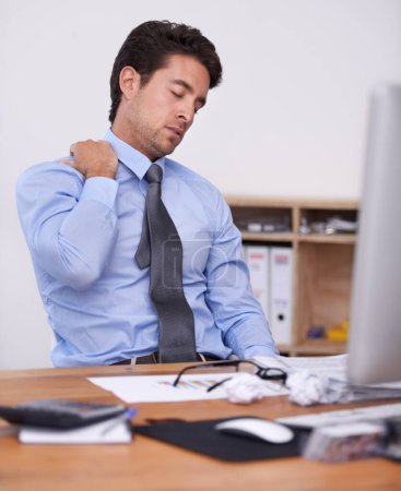 Die Anstrengung spüren. ein müde wirkender junger Geschäftsmann sitzt in seinem Büro