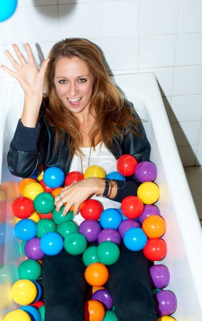 Foto de Todo se trata de divertirse... Atractiva joven hipster chica acostada en una bañera de coloridas bolas de plástico - Imagen libre de derechos