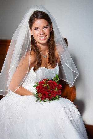 Téléchargez les photos : Prête pour ses noces. Portrait d'une belle jeune mariée assise sur un banc tenant un bouquet de roses - en image libre de droit