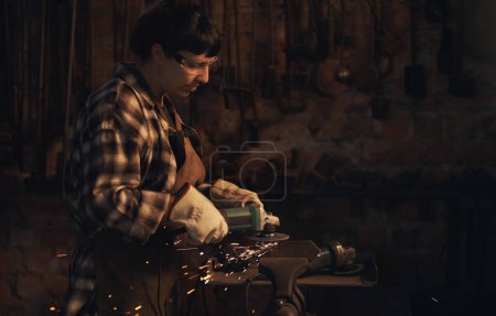 Foto de Hace cosas increíbles con el metal. una mujer joven usando una amoladora angular mientras trabaja en una fundición - Imagen libre de derechos