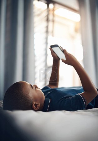 Foto de Este es mi favorito. un niño usando un celular mientras está acostado en su cama - Imagen libre de derechos
