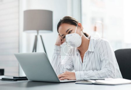 Photo for The world isnt well and everyone is feeling it. a masked young businesswoman looking unhappy while working at her desk in a modern office - Royalty Free Image