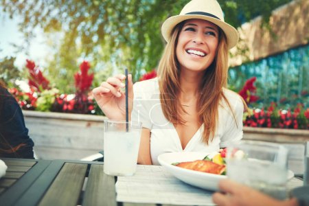 Foto de Qué gran compañía tengo. una joven alegre vistiendo un sombrero y disfrutando de una bebida fría mientras se sienta en un restaurante al aire libre durante el día - Imagen libre de derechos