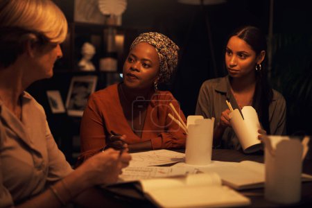 Photo for Lets finish our food, then finish the plan. a group of businesswomen eating takeout while working together in an office at night - Royalty Free Image
