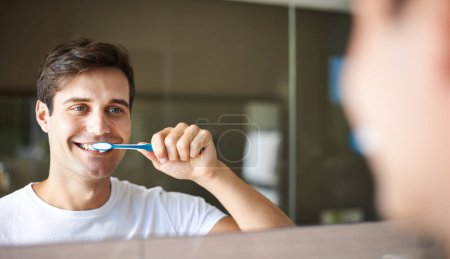 Cepillarse los dientes, el hombre y la limpieza en un baño en casa para la higiene bucal y la salud. Sonrisa, dental y cepillo de dientes con una persona masculina con felicidad en la mañana en una casa con reflejo de espejo.