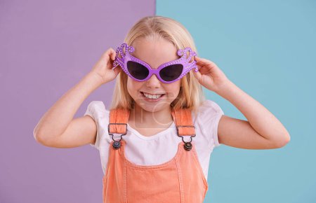 Foto de Extraño y colorido... y eso es sólo su personalidad. Una linda niña usando gafas de sol divertidas contra un fondo colorido - Imagen libre de derechos