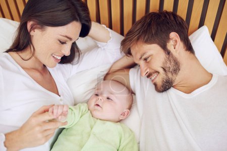 Photo for Top view, parents and smile of baby in bedroom for love, care and quality time together at home. Happy mother, father and family relax with cute newborn kid on bed for support, development and joy. - Royalty Free Image