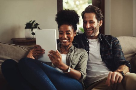 Photo for A love that is all mine. a happy young couple using a digital tablet while relaxing on a couch in their living room at home - Royalty Free Image