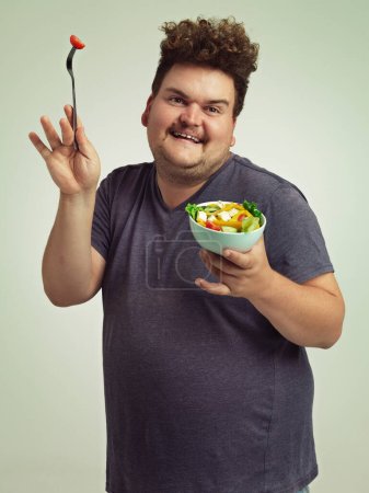 Téléchargez les photos : The salad dance. Studio shot of an overweight man holding a bowl of salad in a silly pose - en image libre de droit