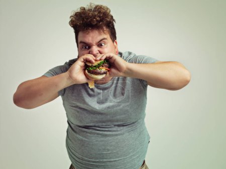 Foto de Es la mejor hamburguesa del mundo. Estudio de un hombre con sobrepeso mordiendo una hamburguesa - Imagen libre de derechos