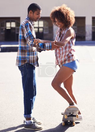 Téléchargez les photos : Il est temps de monter sur ce tableau. un jeune homme enseignant à sa petite amie comment skater - en image libre de droit