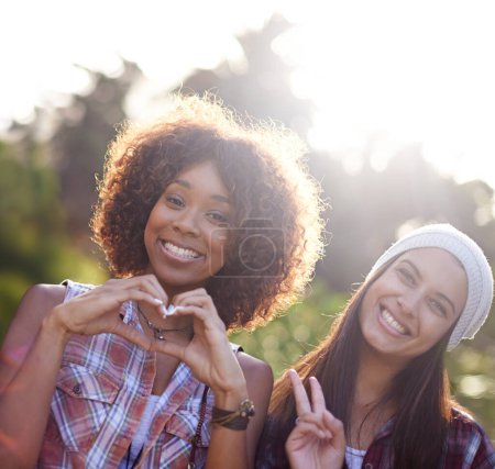 Téléchargez les photos : Paix, amour et bonheur. Une jeune femme fait une forme de cœur avec ses mains tout en se tenant à côté de son ami à l'extérieur - en image libre de droit