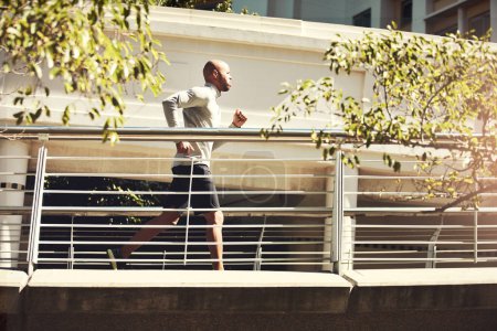 Photo for Your body is important, take care of it with exercise. a handsome young man running on a bridge in the city - Royalty Free Image