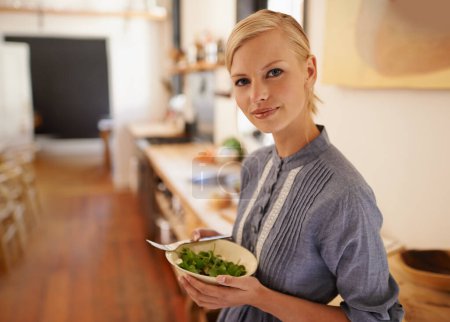 Photo for I always eat healthy. Portrait of a young woman holding a bowl full of leafy greens in a rustic kitchen - Royalty Free Image