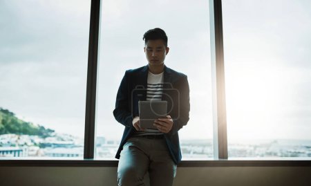 Foto de La forma inteligente de mantenerse al día con las tendencias empresariales. un joven hombre de negocios usando una tableta digital en una oficina moderna - Imagen libre de derechos