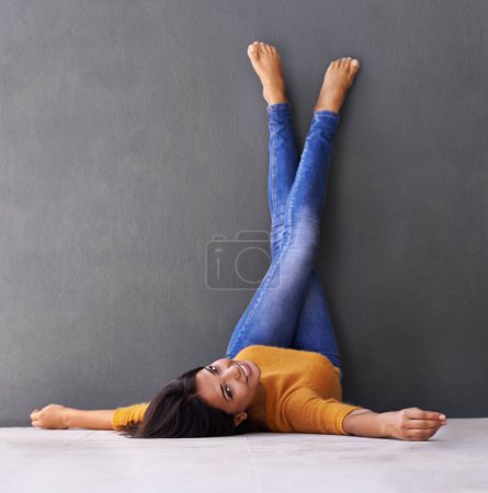 Mastering the art of relaxation. an attractive young woman lying on the floor with her feet against the wall