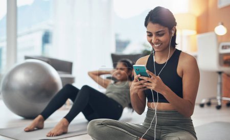 Photo for This app has good music and great exercises to go with it. a woman listening to music through her cellphone while exercising at home - Royalty Free Image