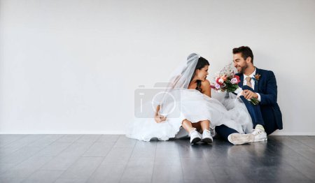 Téléchargez les photos : Comme tu es excitée. Plan studio d'un jeune couple nouvellement marié assis par terre sur un fond gris - en image libre de droit