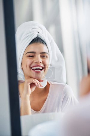 Foto de Me encanta la piel en la que estoy. una hermosa joven limpiando su cara con lana de algodón en el baño en casa - Imagen libre de derechos