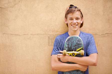 Téléchargez les photos : Son passe-temps après l'école. Portrait d'un adolescent tenant son skateboard debout contre un mur - en image libre de droit