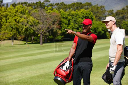 Téléchargez les photos : Le prochain trou est par là. deux hommes portant leurs sacs de golf à travers un terrain de golf et pointant vers quelque chose - en image libre de droit