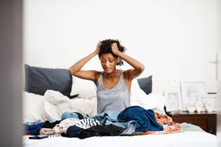 Foto de Tanta ropa, tan poco tiempo. una joven infeliz vistiéndose con montones de ropa en su cama - Imagen libre de derechos
