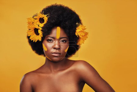 Photo for She serves beauty with confidence. Studio portrait of a beautiful young woman posing topless with sunflowers in her hair against a mustard background - Royalty Free Image