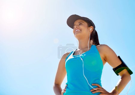 Photo for Running is quality time with me. a young woman listening to music while out for a run against a clear blue sky - Royalty Free Image