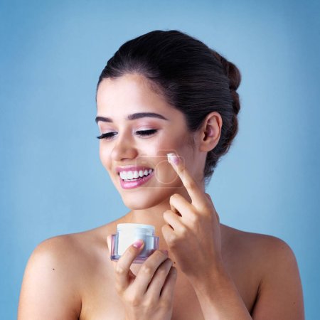 Photo for Give your skin the attention it deserves. Studio shot of a beautiful young woman applying face cream against a blue background - Royalty Free Image