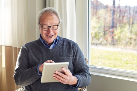 Foto de Feliz cuando descubre cosas nuevas en su dispositivo. un hombre mayor usando una tableta en casa - Imagen libre de derechos